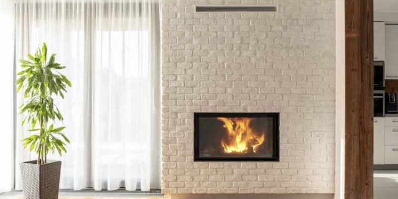 Tall white brick wall with fireplace insert behind well lit room with wood flooring - KreteworX fireplace Idaho Falls ID