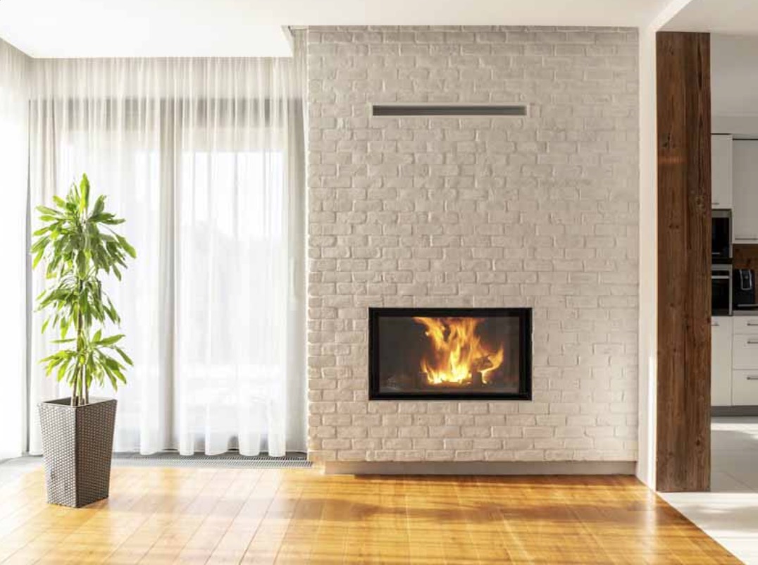 Tall white brick wall with fireplace insert behind well lit room with wood flooring - KreteworX fireplace Idaho Falls ID